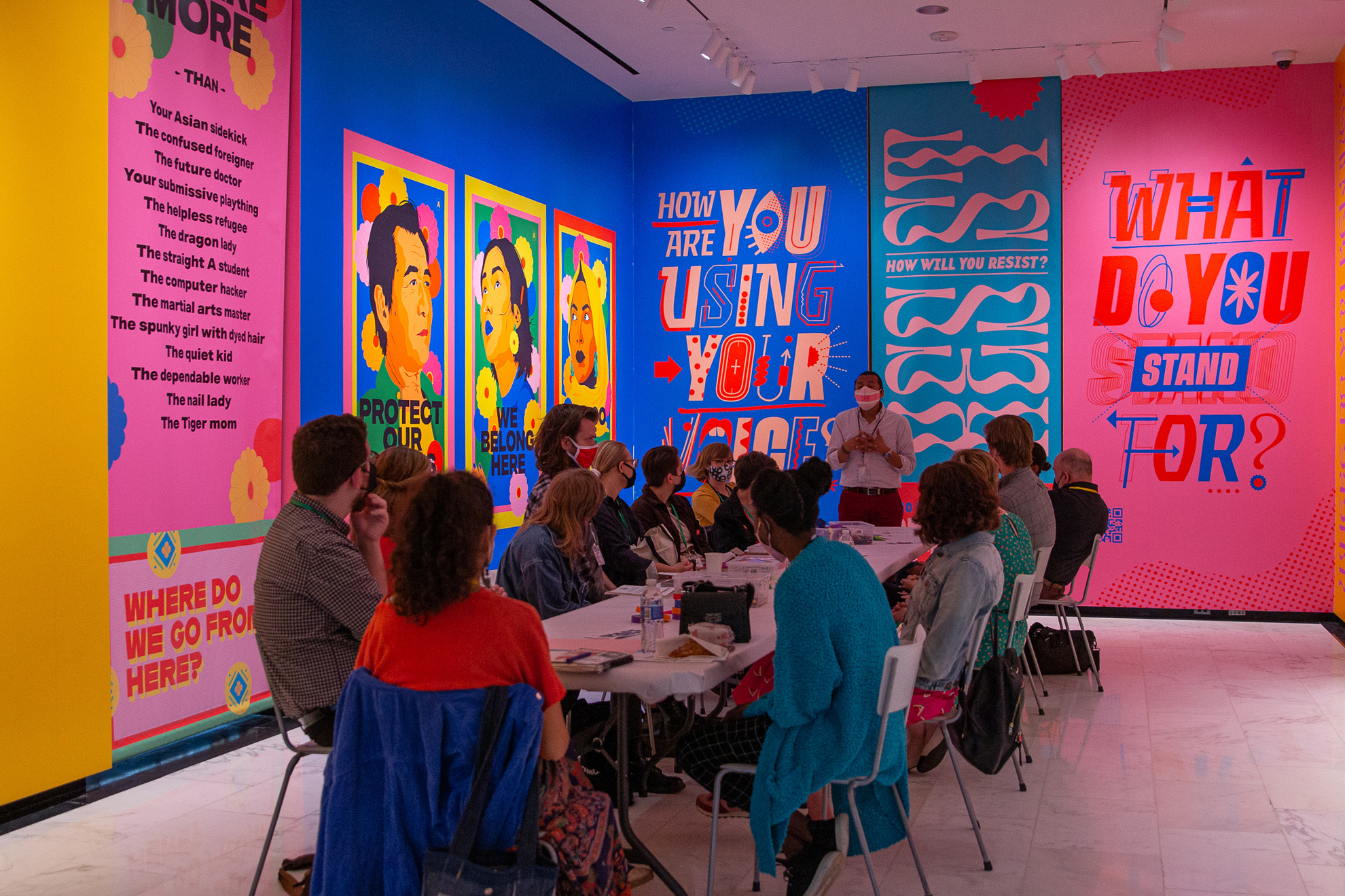 A group of educators sitting around a table listening to a facilitator against a backdrop of a brightly colored mural.
